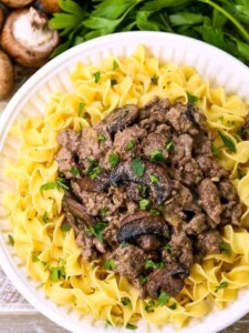 ground beef stroganoff served over noodles on a white diner plate