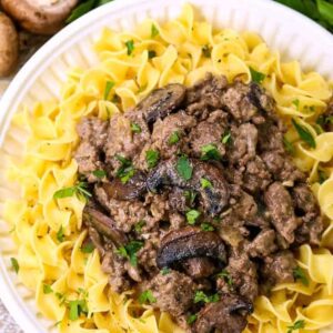 ground beef stroganoff served over noodles on a white diner plate