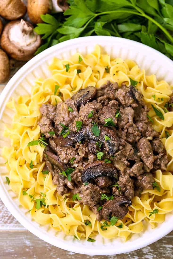 ground beef stroganoff served over noodles on a white diner plate