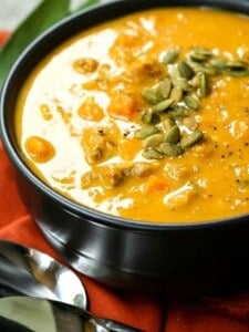 pumpkin sausage soup in a black bowl with pumpkin seeds