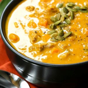 pumpkin sausage soup in a black bowl with pumpkin seeds