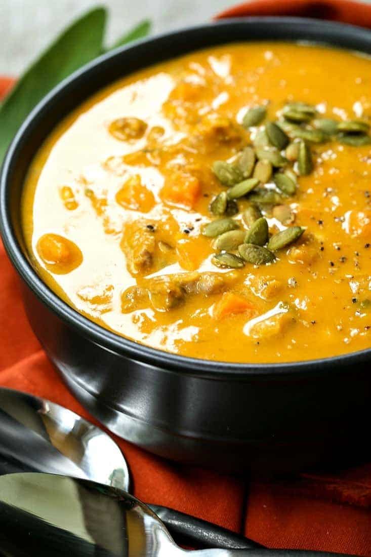 pumpkin sausage soup in a black bowl with pumpkin seeds