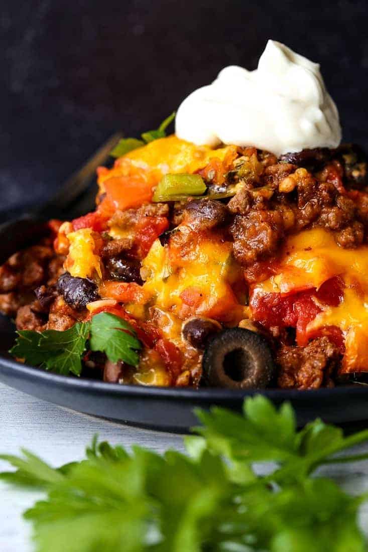 This Taco Casserole Recipe brings the party to dinner time! Loaded with seasoned ground beef, beans and cheese, your friends and family are going to come running to the dinner table! taco casserole on a black plate with sour cream