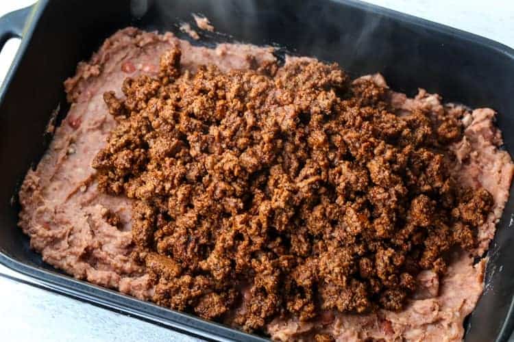 This Taco Casserole Recipe brings the party to dinner time! Loaded with seasoned ground beef, beans and cheese, your friends and family are going to come running to the dinner table! taco casserole in a black baking dish
