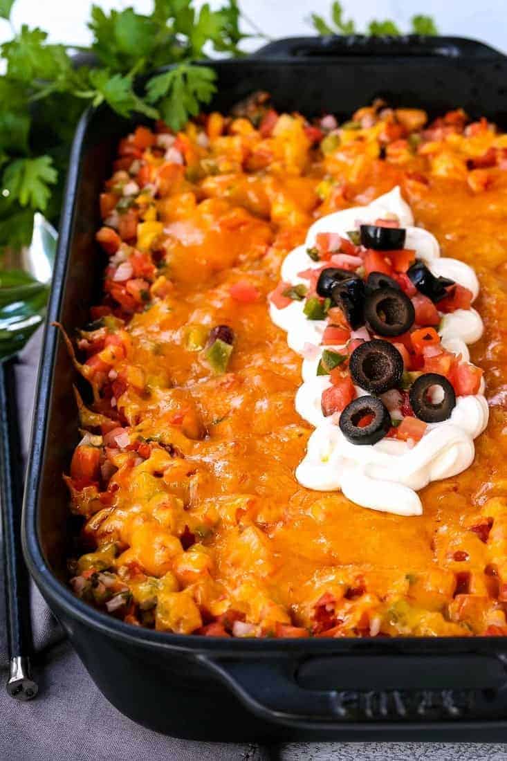 fiesta taco casserole in a black baking dish with sour cream and olives