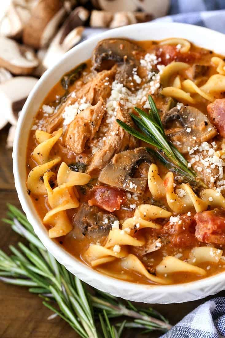 chicken and noodle soup with mushrooms in a bowl with fresh rosemary