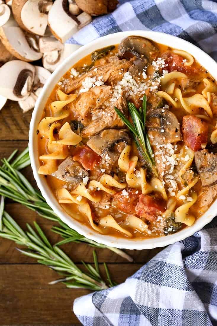 chicken soup with spinach and mushrooms in a bowl with rosemary and a checkered napkin