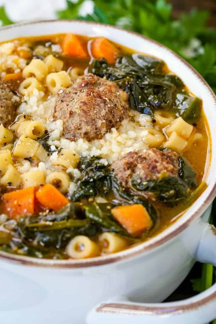 soup in a white crock with meatballs, pasta and spinach