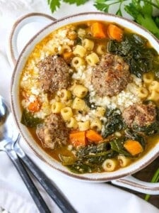 italian wedding soup in a white bowl with black spoons