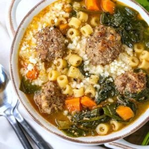italian wedding soup in a white bowl with black spoons