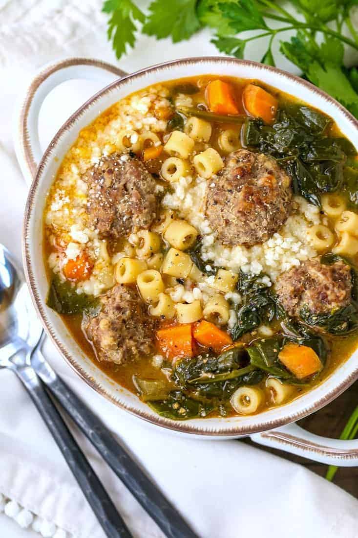 italian wedding soup in a white bowl with black spoons