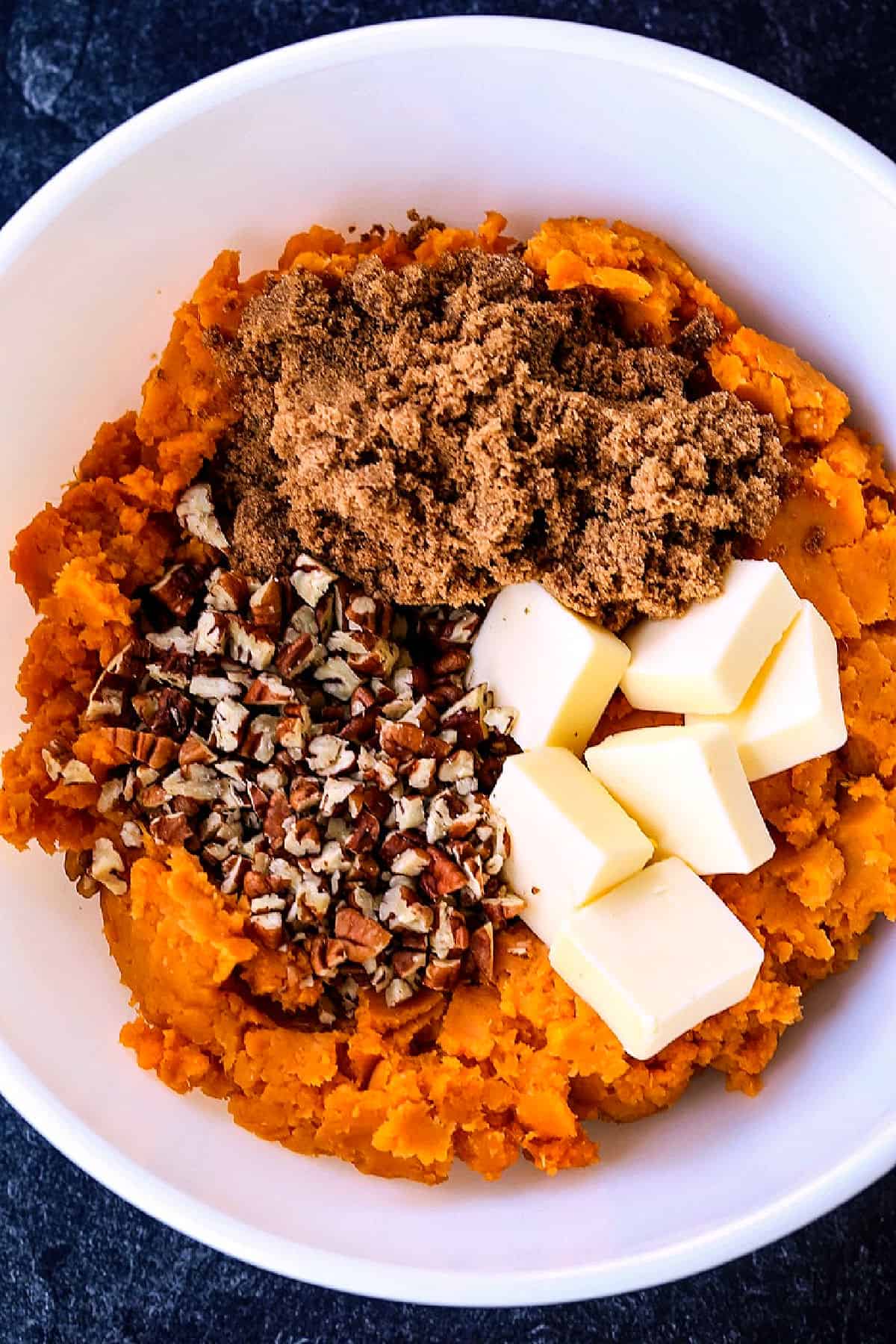 mashed sweet potatoes, brown sugar, nuts and butter in a white bowl
