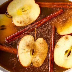 apple cider in a slow cooker with apple slices and cinnamon sticks