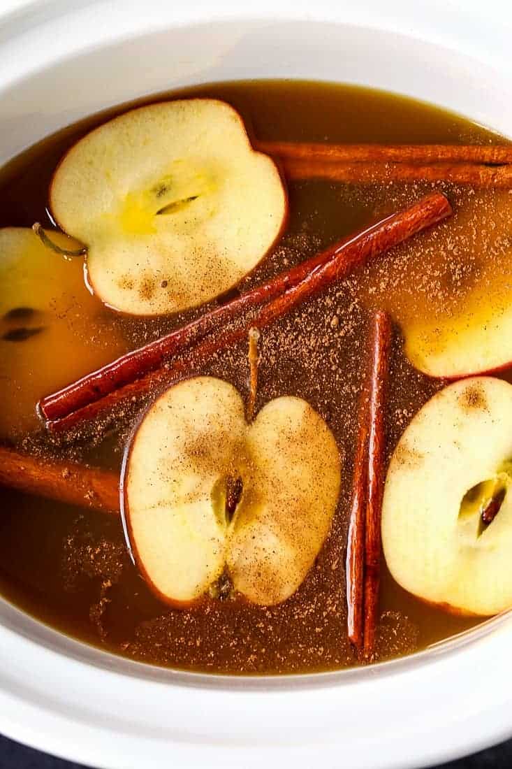 apple cider in a slow cooker with apple slices and cinnamon sticks