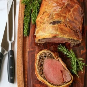 A slice of beef wellington on a board beside the remaining pastry-wrapped tenderloin.