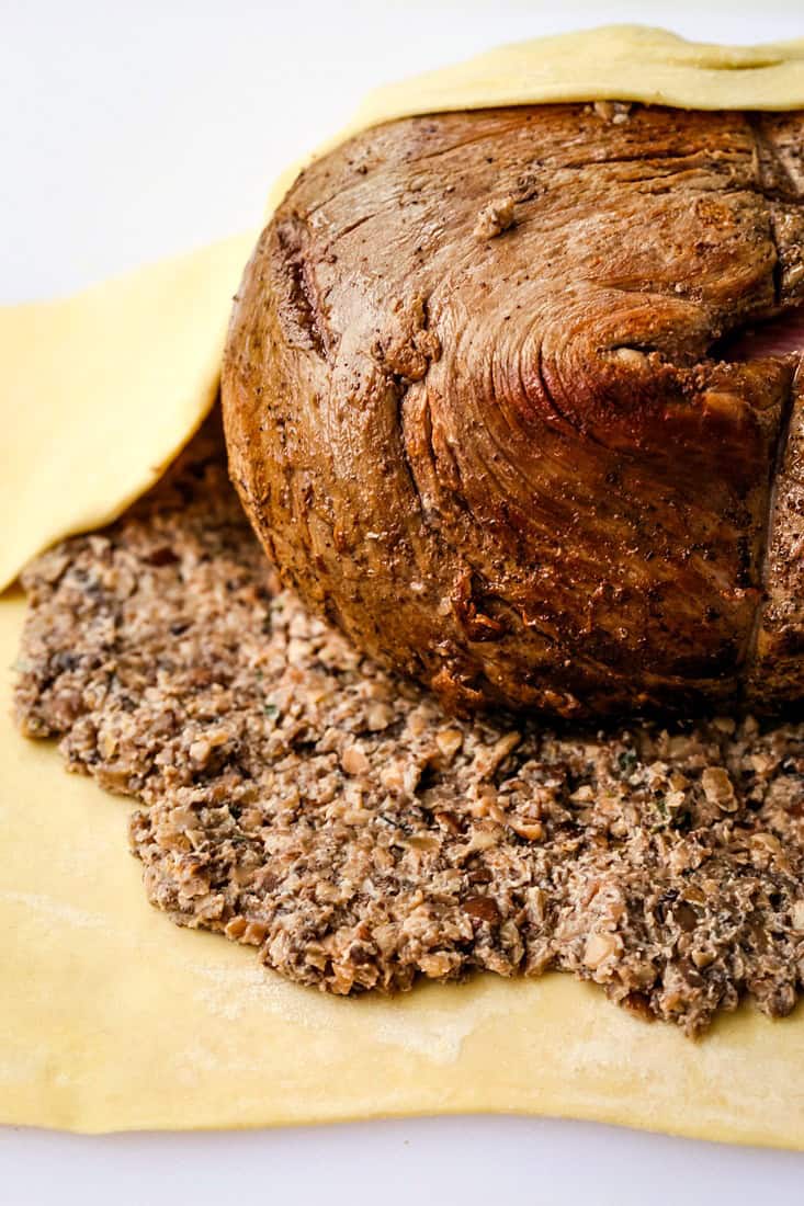 Roasted beef tenderloin being wrapped in mushroom duxelle and puff pastry.