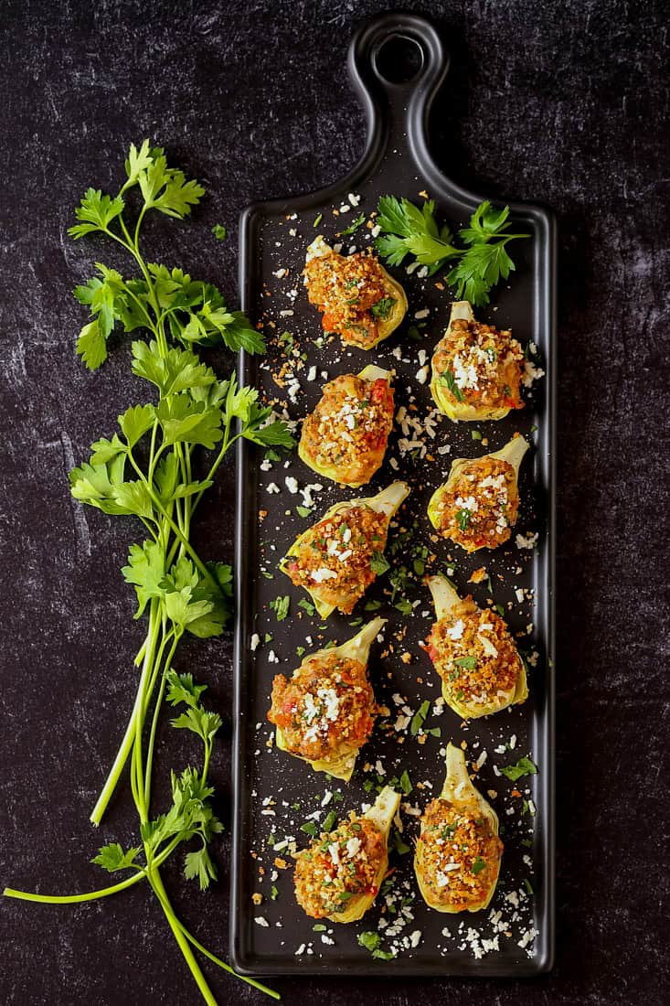 artichoke hearts stuffed with sausage and sun dried tomatoes on a black platter