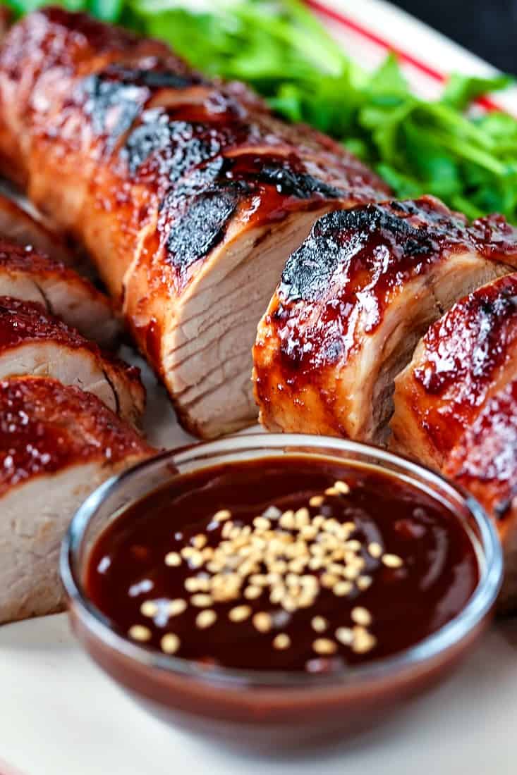 sliced pork tenderloin recipe with a cup of sauce and sesame seeds