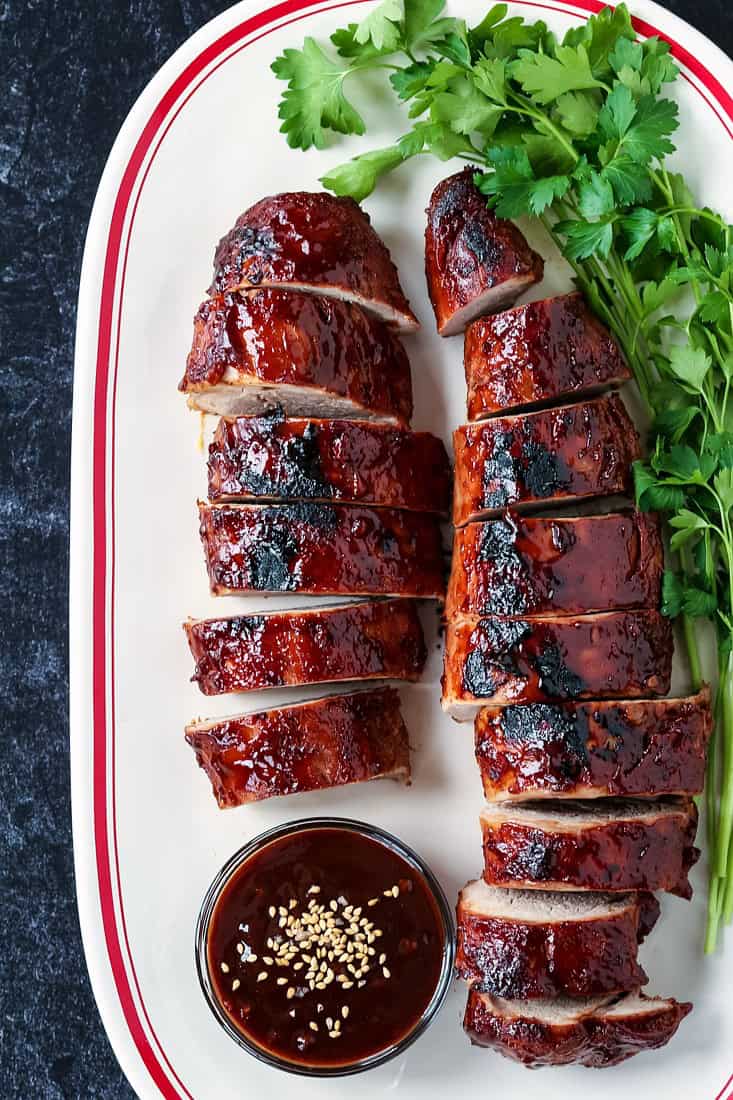 bbq pork tenderloin sliced on a white platter with sauce