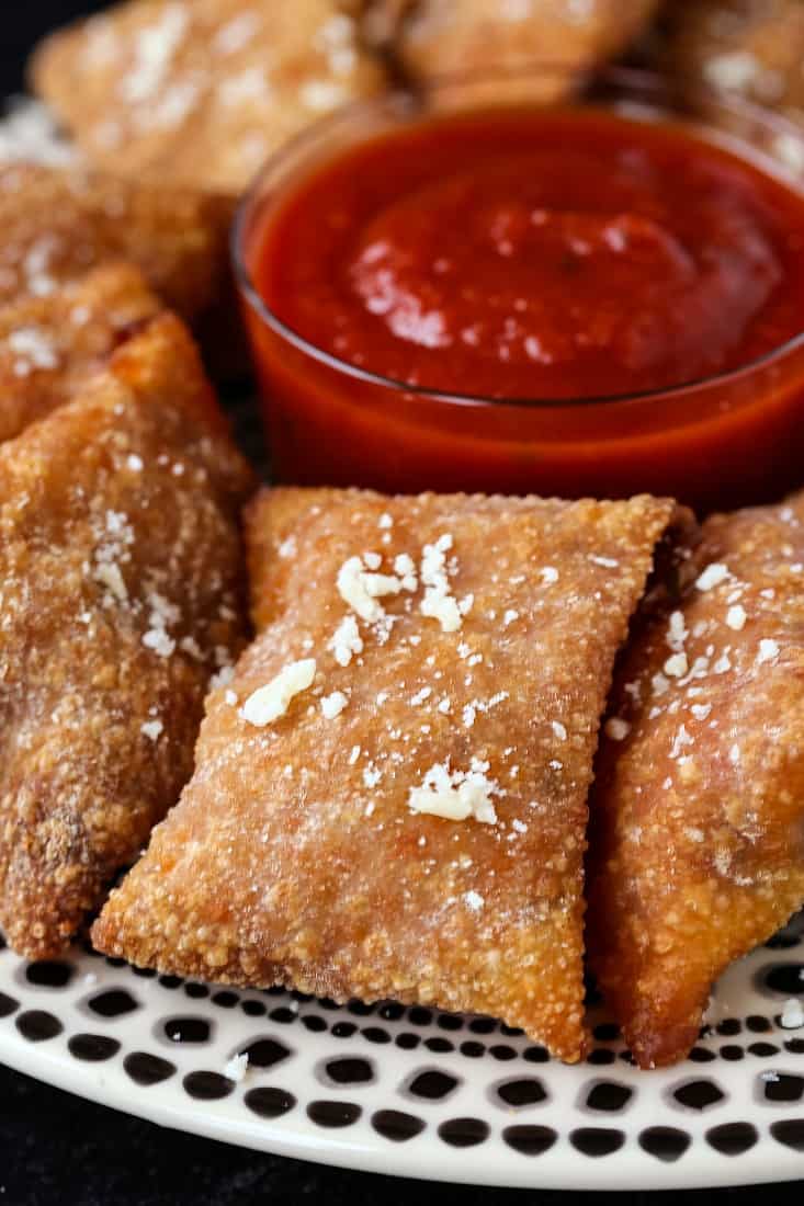 A close-up of a Copycat Totino's Pizza Roll arranged with others on a plate around a small dish of tomato sauce.