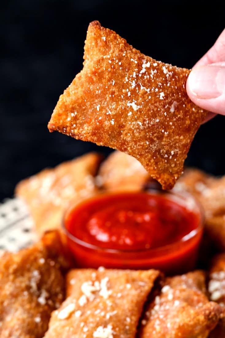 Someone lifting a crispy pizza roll sprinkled with parmesan cheese from a plate of pizza rolls.