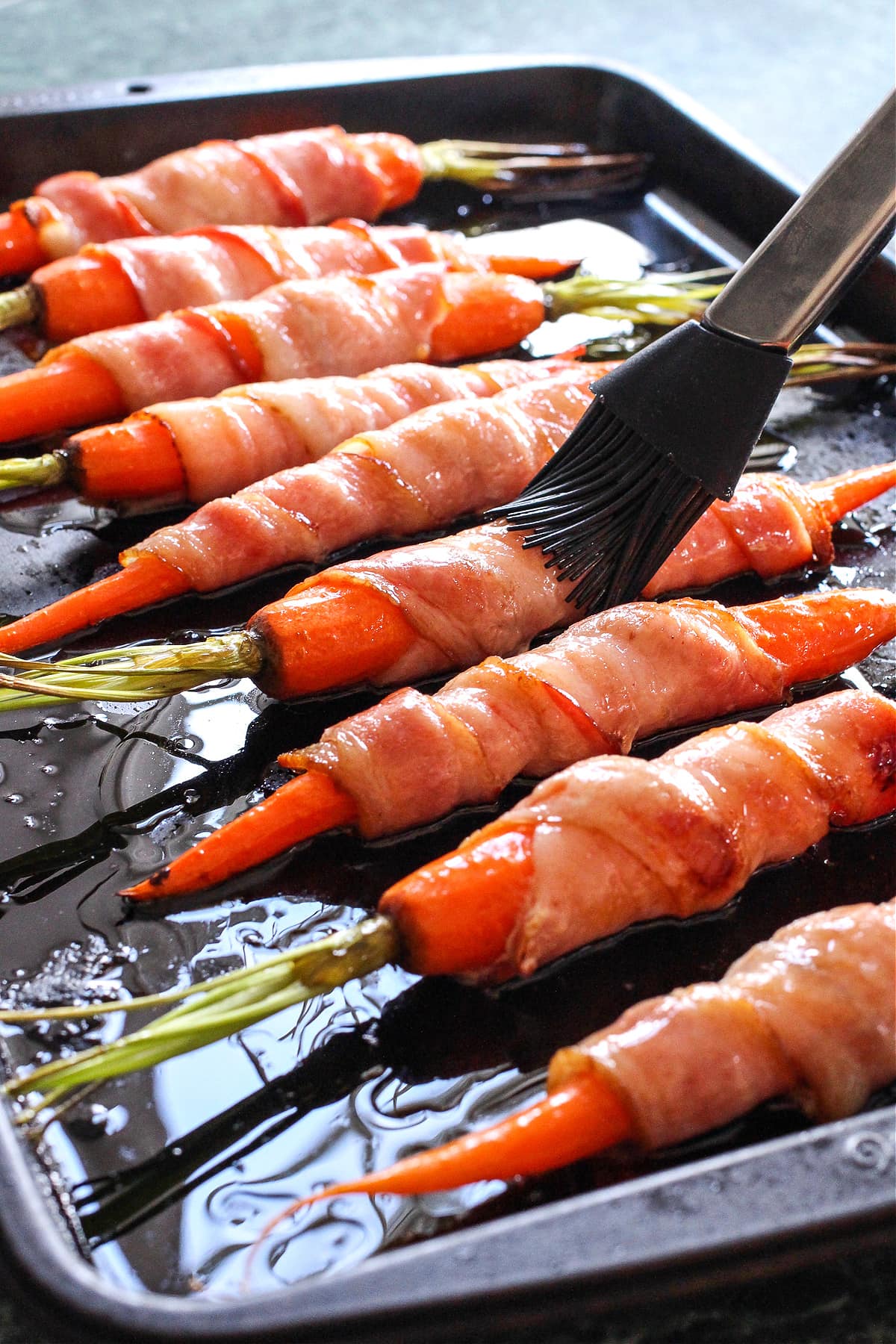 glaze being brushed on carrots wrapped with bacon