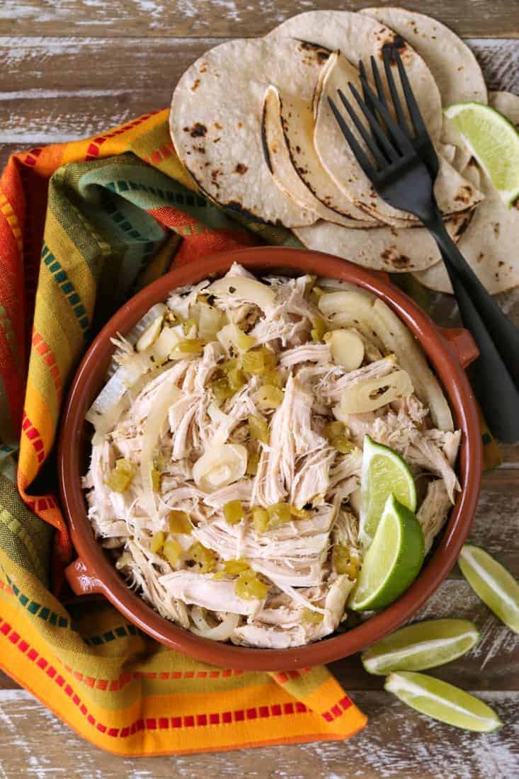 Slow Cooker Mexican Chicken is so full of flavor with just a few ingredients! Use this chicken for tacos, burritos, nachos, salads and more! Shredded chicken in a bowl with limes