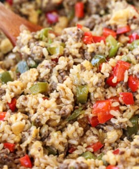 cheesy rice with ground beef and peppers in skillet with wooden spoon
