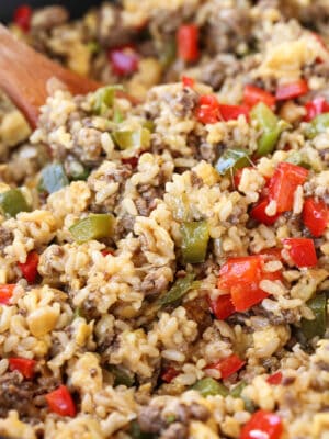 cheesy rice with ground beef and peppers in skillet with wooden spoon