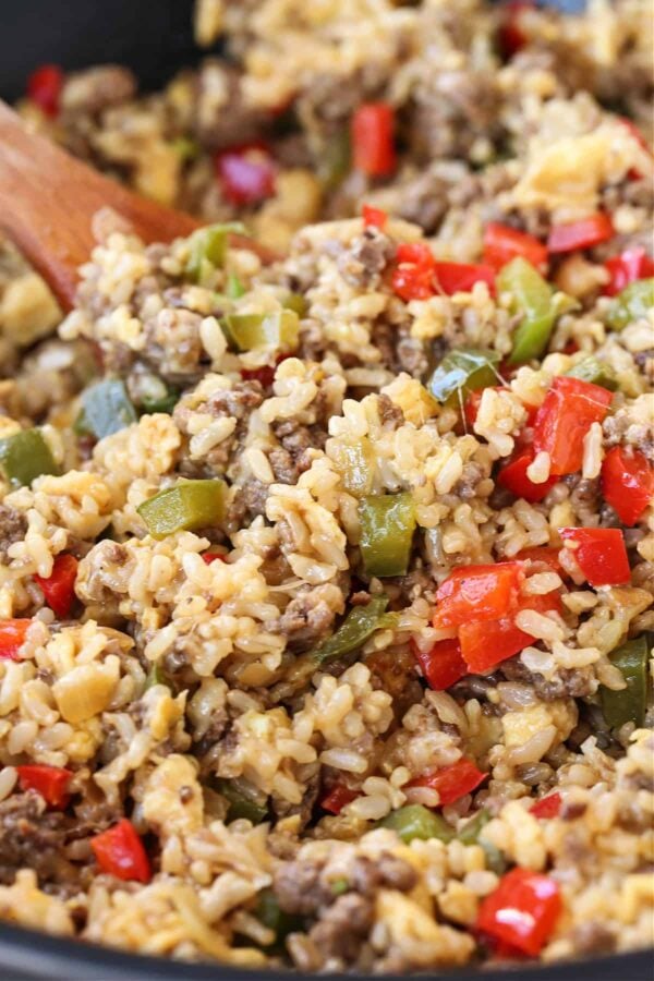 cheesy rice with ground beef and peppers in skillet with wooden spoon