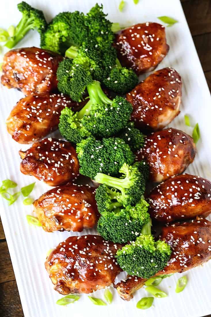 Baked chicken legs with an Asian glaze on a white platter with broccoli