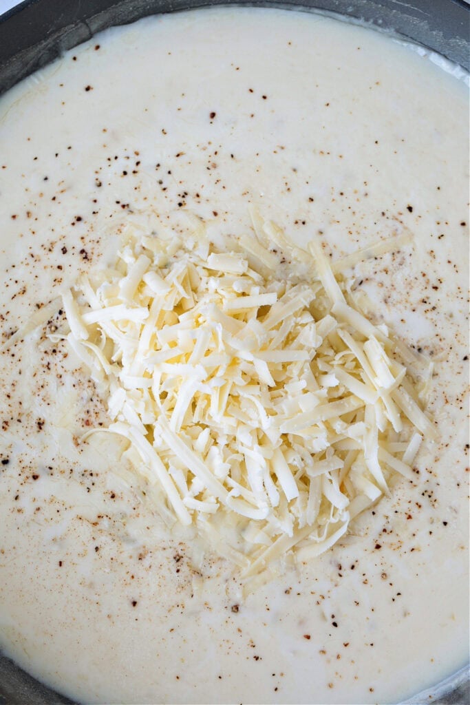 Cheesy Green Bean Casserole is sure to be a favorite Thanksgiving side dish! A scratch made cheesy cream sauce makes all the difference! grated cheese in a skillet with cream sauce