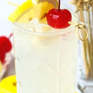 A Tom Collins cocktail with a lemon wedge and a cherry for garnish