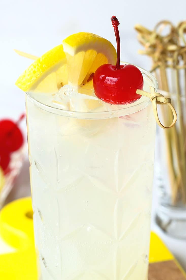 A Tom Collins cocktail with a lemon wedge and a cherry for garnish