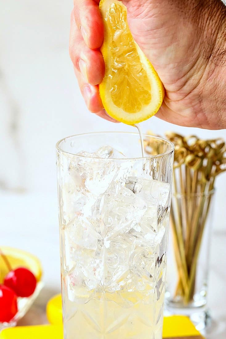 A Tom Collins Cocktail Recipe is a delicious gin drink with fresh lemon juice and seltzer! A refreshing cocktail for any time of the year! Fresh lemon juiced being squeezed into a glass to make a Tom Collins