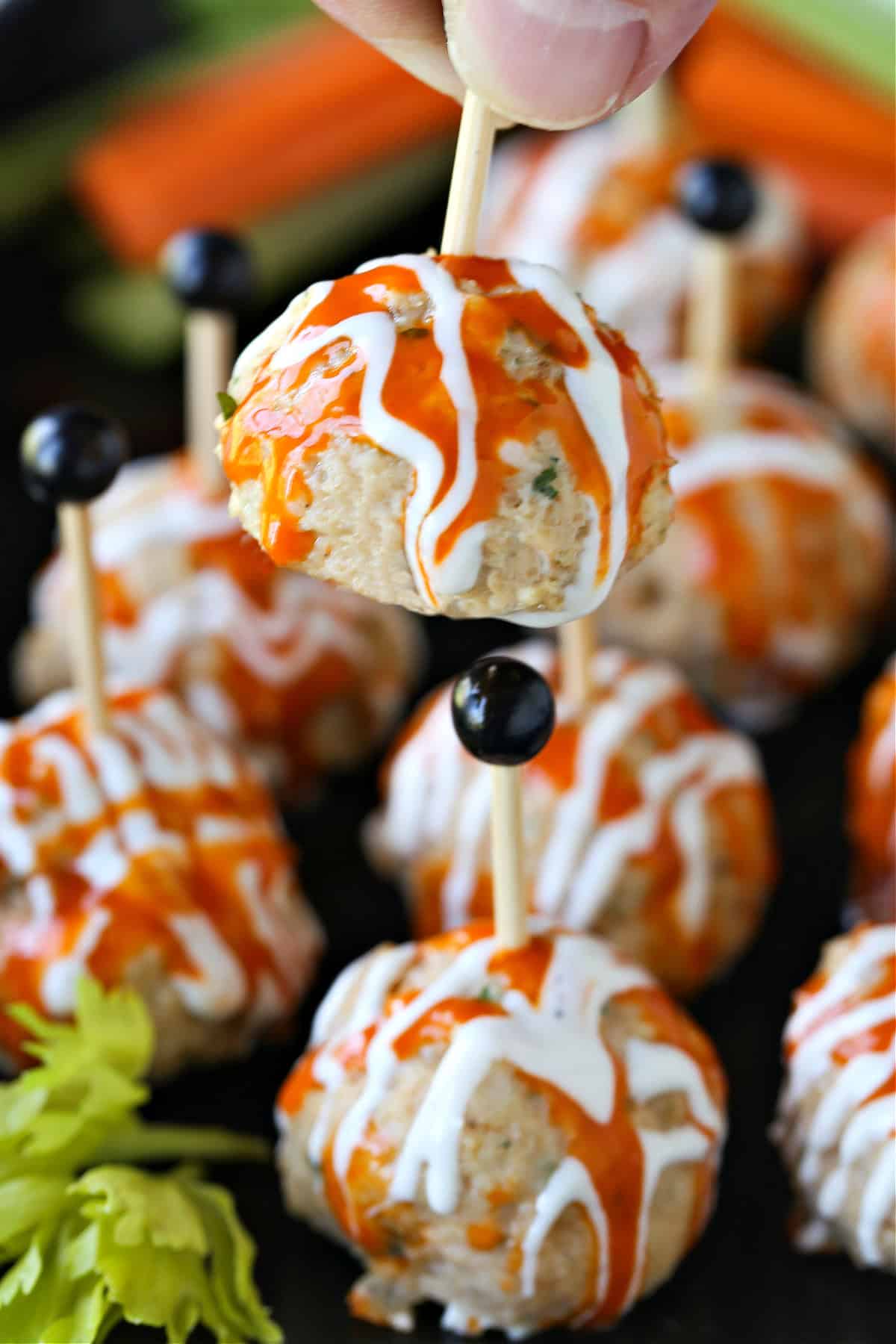 holding a chicken meatball with buffalo and blue cheese sauce drizzle