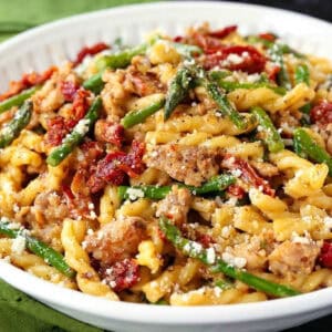 pasta with italian sausage, sun dried tomatoes and asparagus in a white bowl