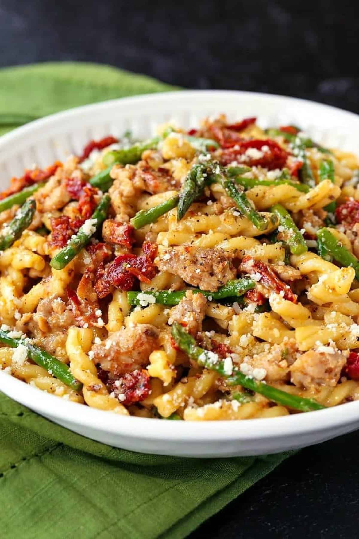 Gemelli with Sausage and Asparagus is light yet full of flavor. Zesty Italian sausage and crisp asparagus tossed in a light white wine sauce. pasta with italian sausage, sun dried tomatoes and asparagus in a white bowl