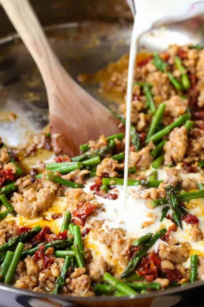 Gemelli with Sausage and Asparagus is light yet full of flavor. Zesty Italian sausage and crisp asparagus tossed in a light white wine sauce. cream pouring into a skillet with sausage and vegetables