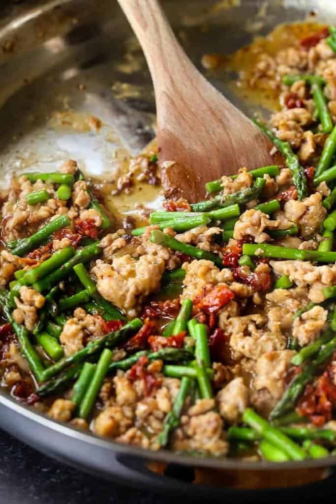 Gemelli with Sausage and Asparagus is light yet full of flavor. Zesty Italian sausage and crisp asparagus tossed in a light white wine sauce. sausage, asparagus and sun dried tomatoes in skillet with wooden spoon