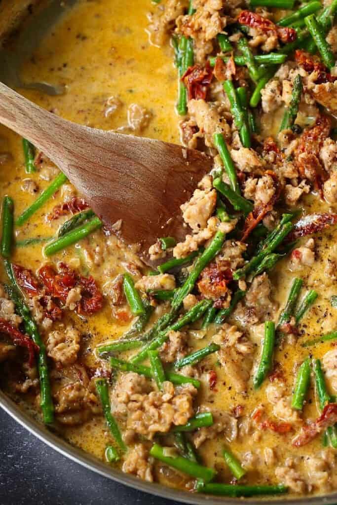 Gemelli with Sausage and Asparagus is light yet full of flavor. Zesty Italian sausage and crisp asparagus tossed in a light white wine sauce. pasta sauce in skillet with asparagus and sausage