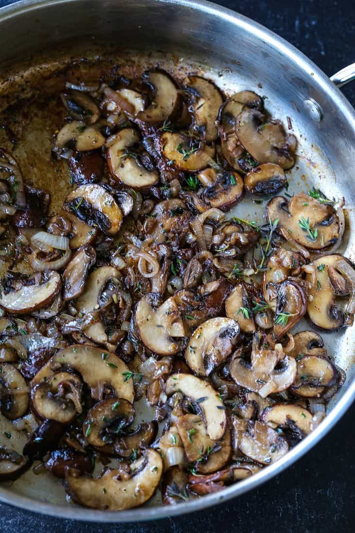 Mushrooms cooking in a skillet with fresh thyme and shallots