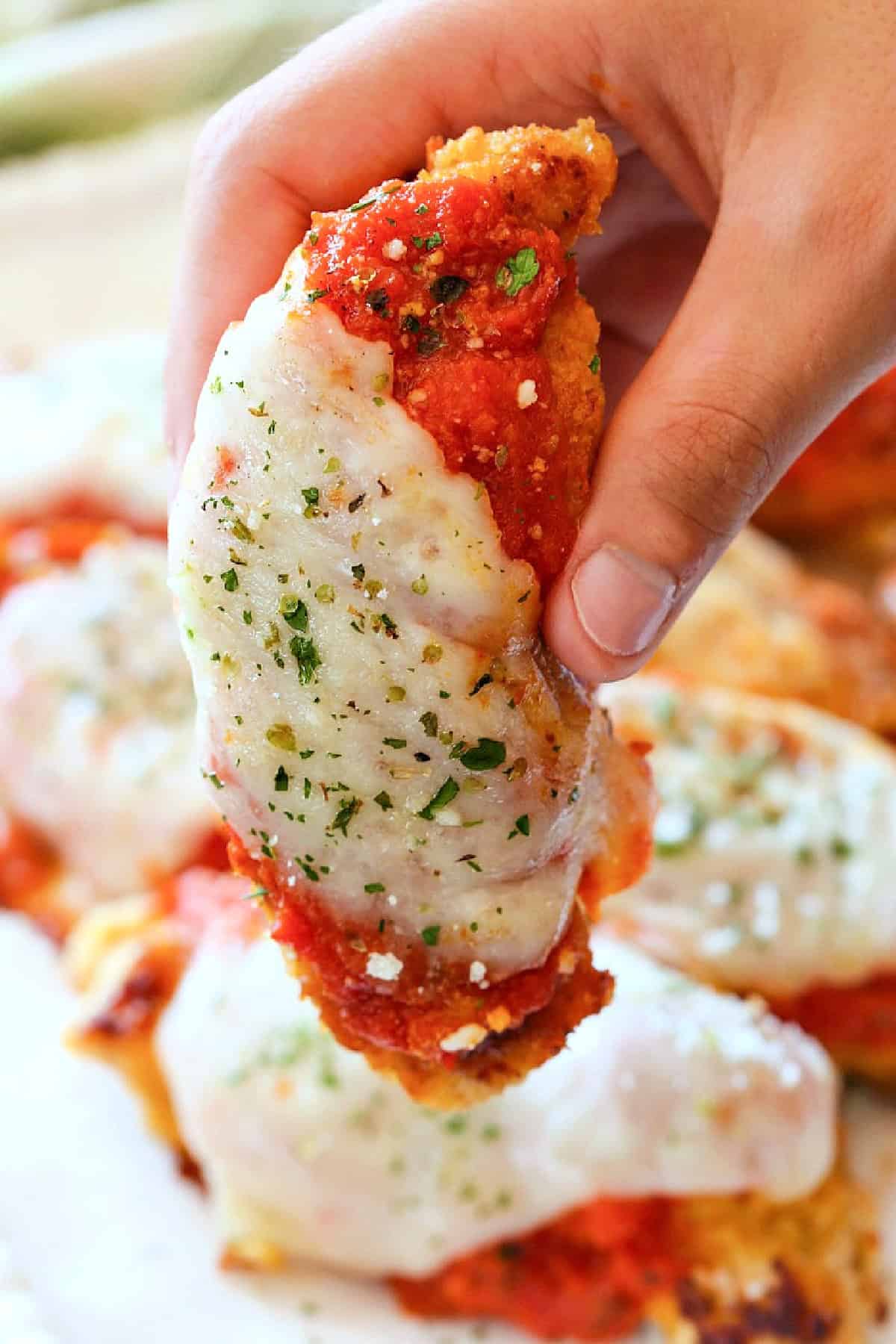 hand holding a chicken tenderloin with sauce and mozzarella cheese