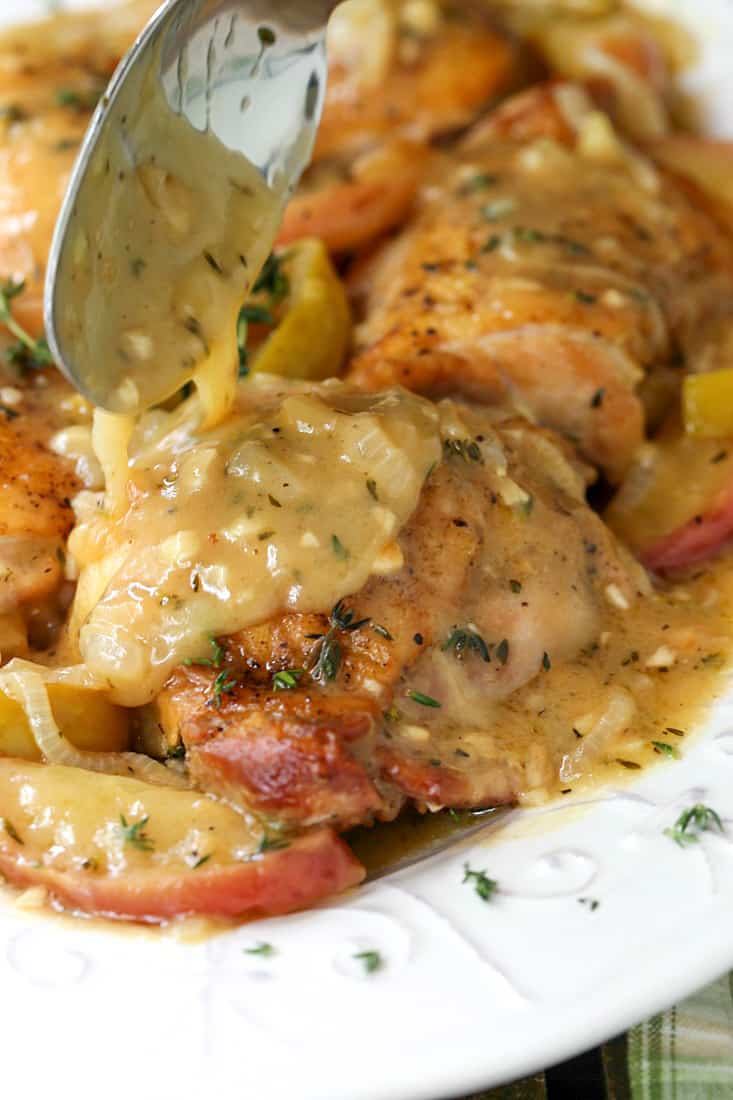 Gravy being spooned over chicken thighs with apples