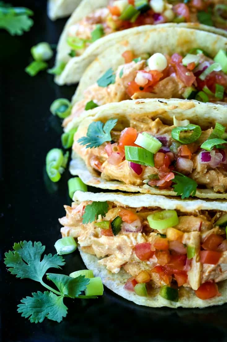 Crock pot salsa chicken in taco shells topped with veggies on a black plate.