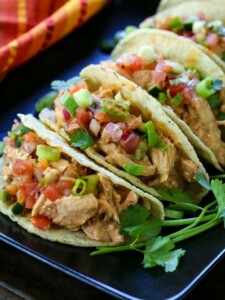 A row of tacos filled with creamy salsa chicken and topped with fresh vegetables.