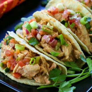 A row of tacos filled with creamy salsa chicken and topped with fresh vegetables.