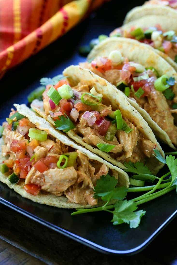 A row of tacos filled with creamy salsa chicken and topped with fresh vegetables.