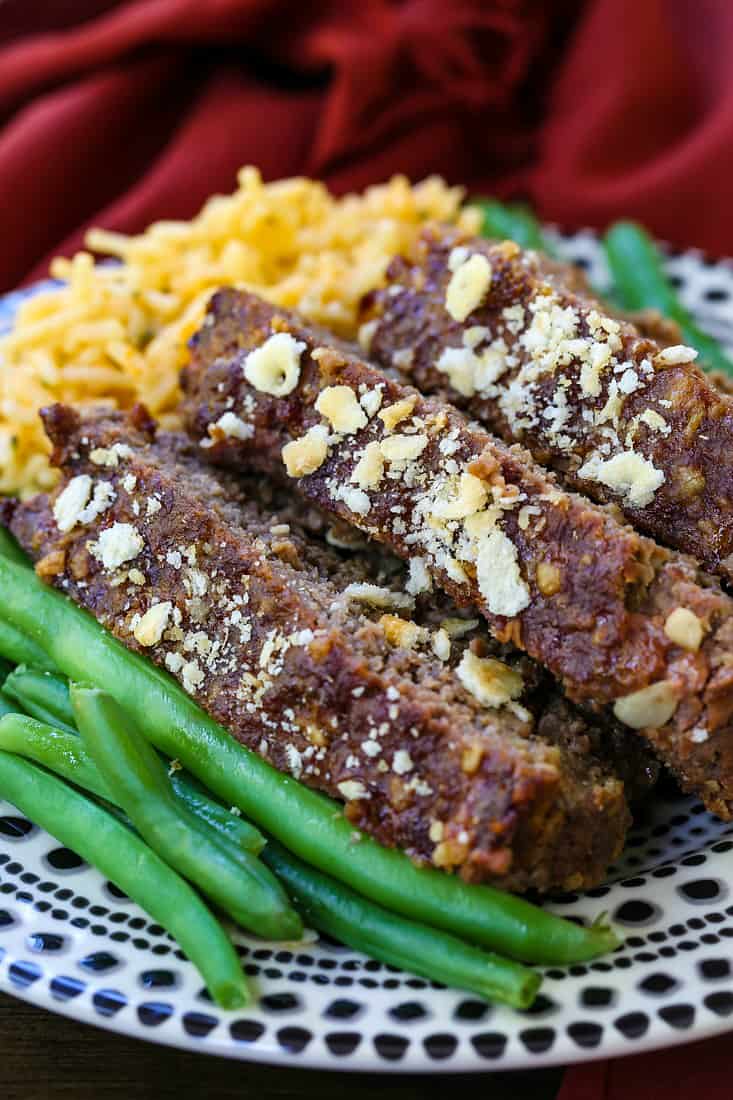 Slices of meatloaf stacked on a plate with green beans