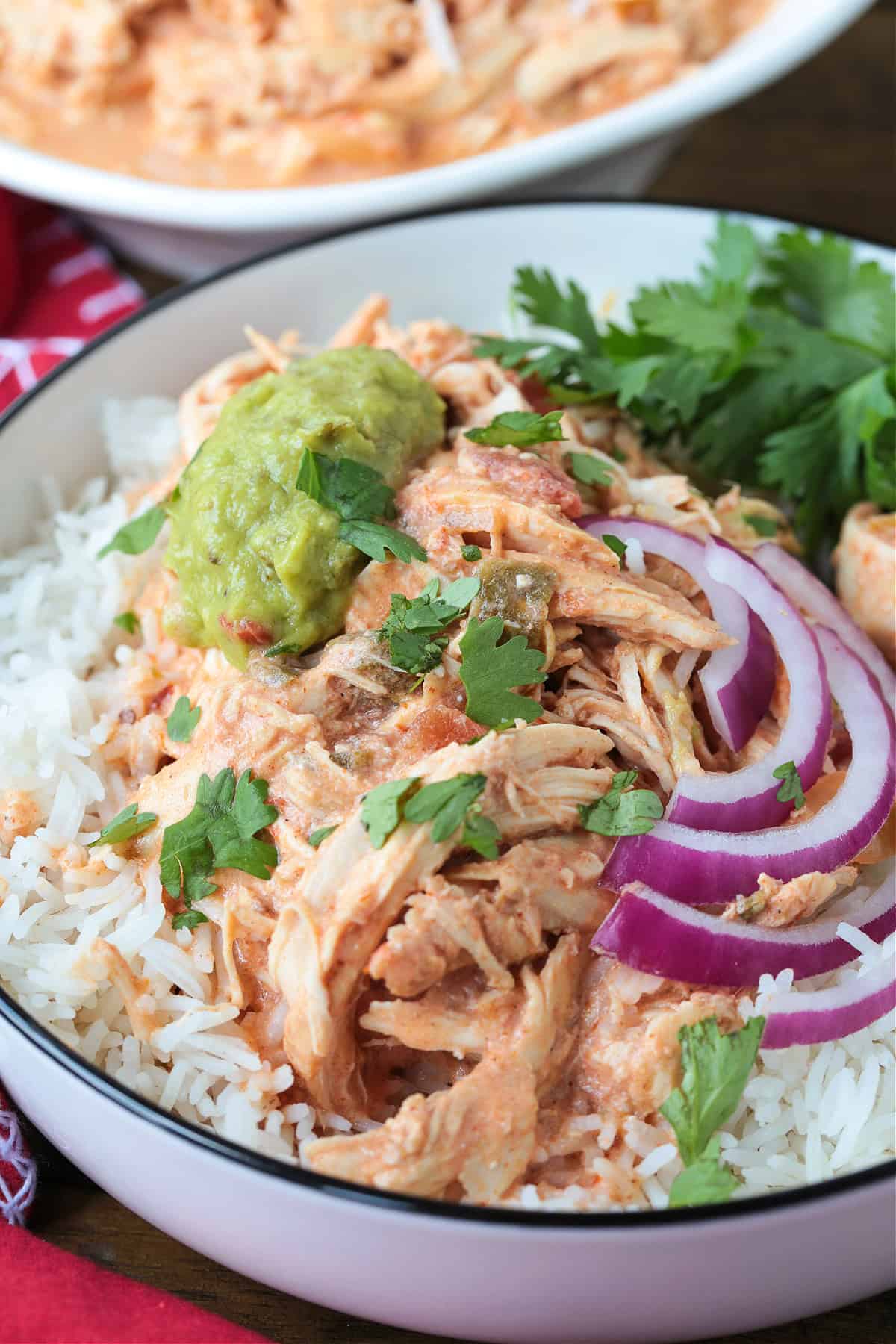 bowl with rice and shredded salsa chicken topped with sliced onions and guacamole